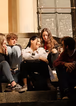 Groupe d'adolescents assis sur des marches en conversation près d'un mur et d'une fenêtre.
