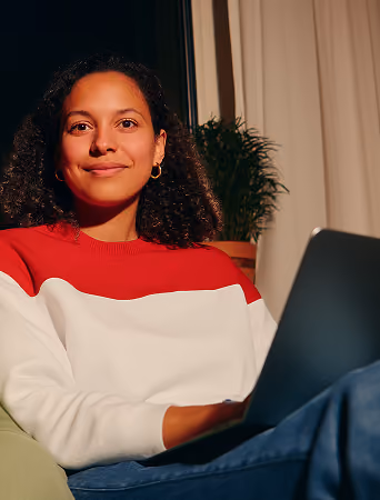 Jeune femme souriante portant un pull rouge et blanc assise avec un ordinateur portable.