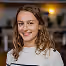 Jeune femme souriante avec cheveux bouclés et chandail blanc, fond flou intérieur.
