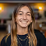 Jeune femme souriante aux cheveux longs blonds portant un collier et un haut noir.