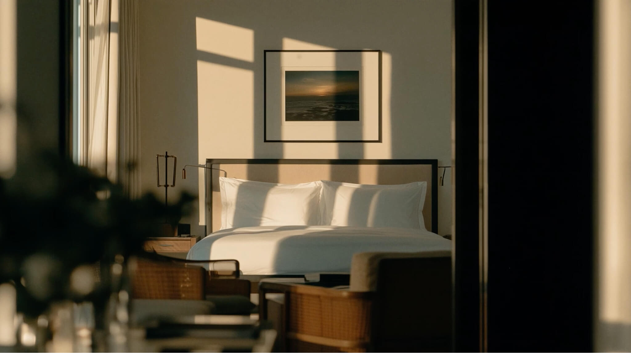 Modern bedroom with sunlit bed, framed sunset artwork, wooden nightstands, and minimalist decor.