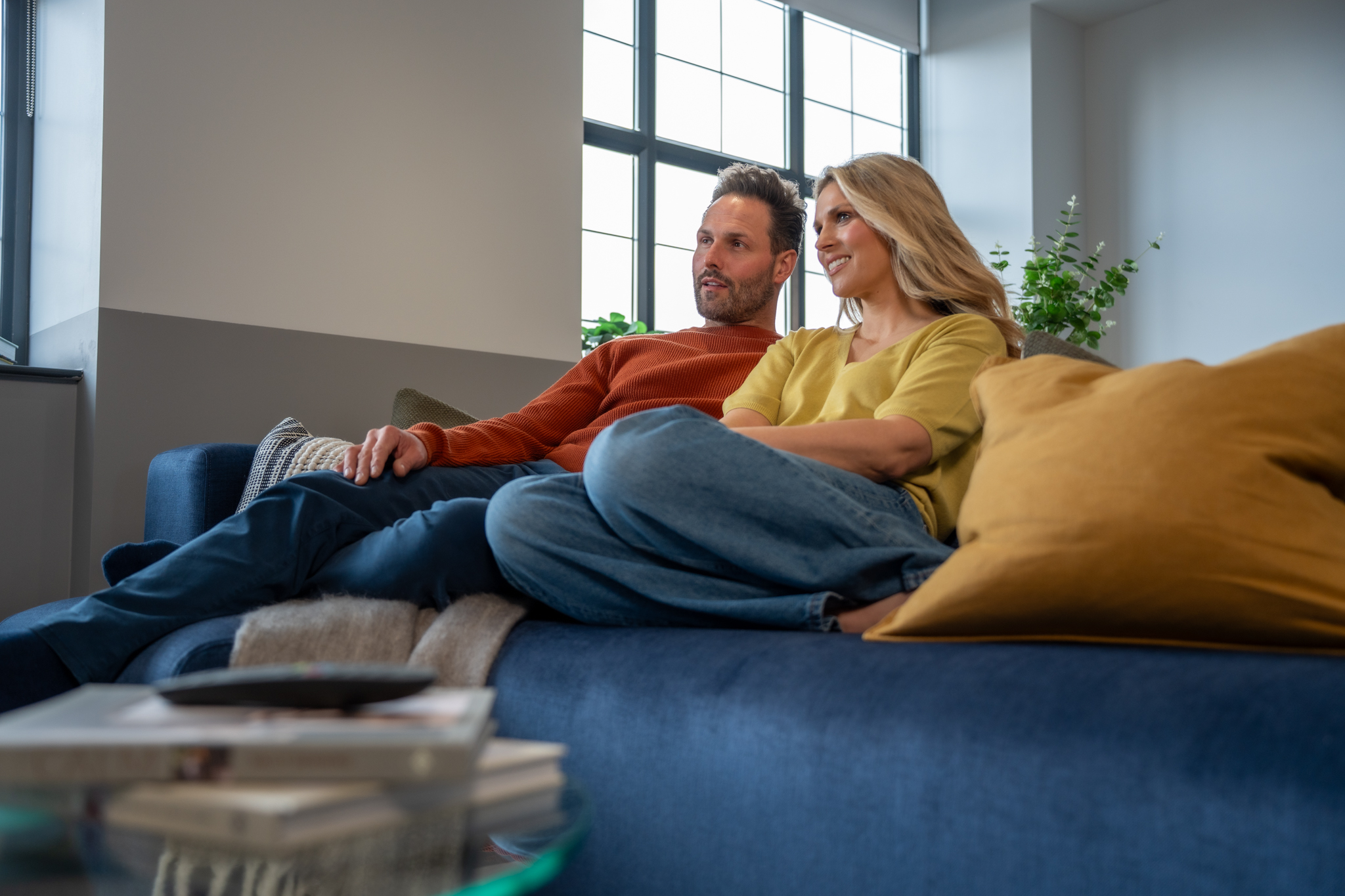 A couple relaxing together on a sofa inside a modern Paragon Living apartment, enjoying a bright open living space with large windows and contemporary furnishings.