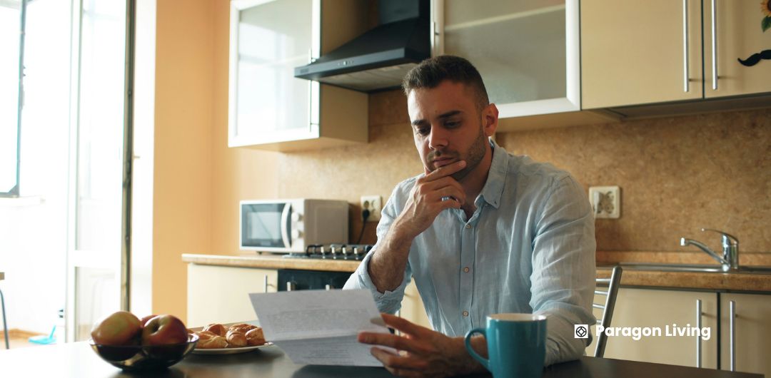 Man sitting at a kitchen table, writing notes on paper about common mistakes first-time renters make.