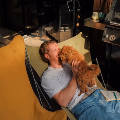 A Nutchel guest cuddling with his dog on the terrace of his cabin in the woods in Belgium