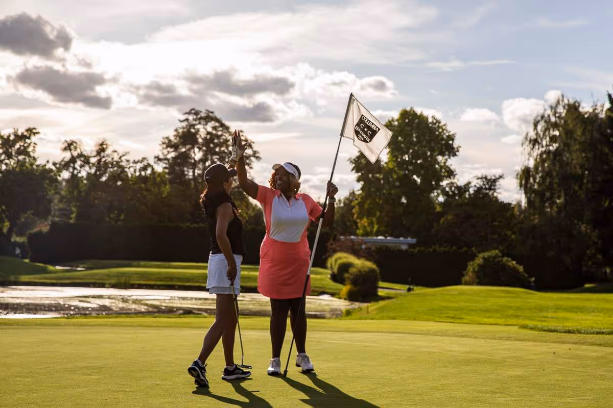 Two women golfers high-five on a green after making a shot