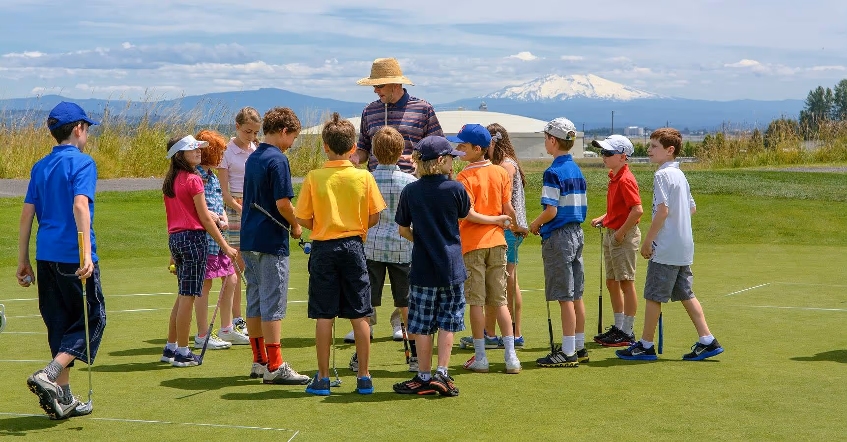Group of junior golfers surround an instructor on the practice greens while Mt Hood looms on the horizon