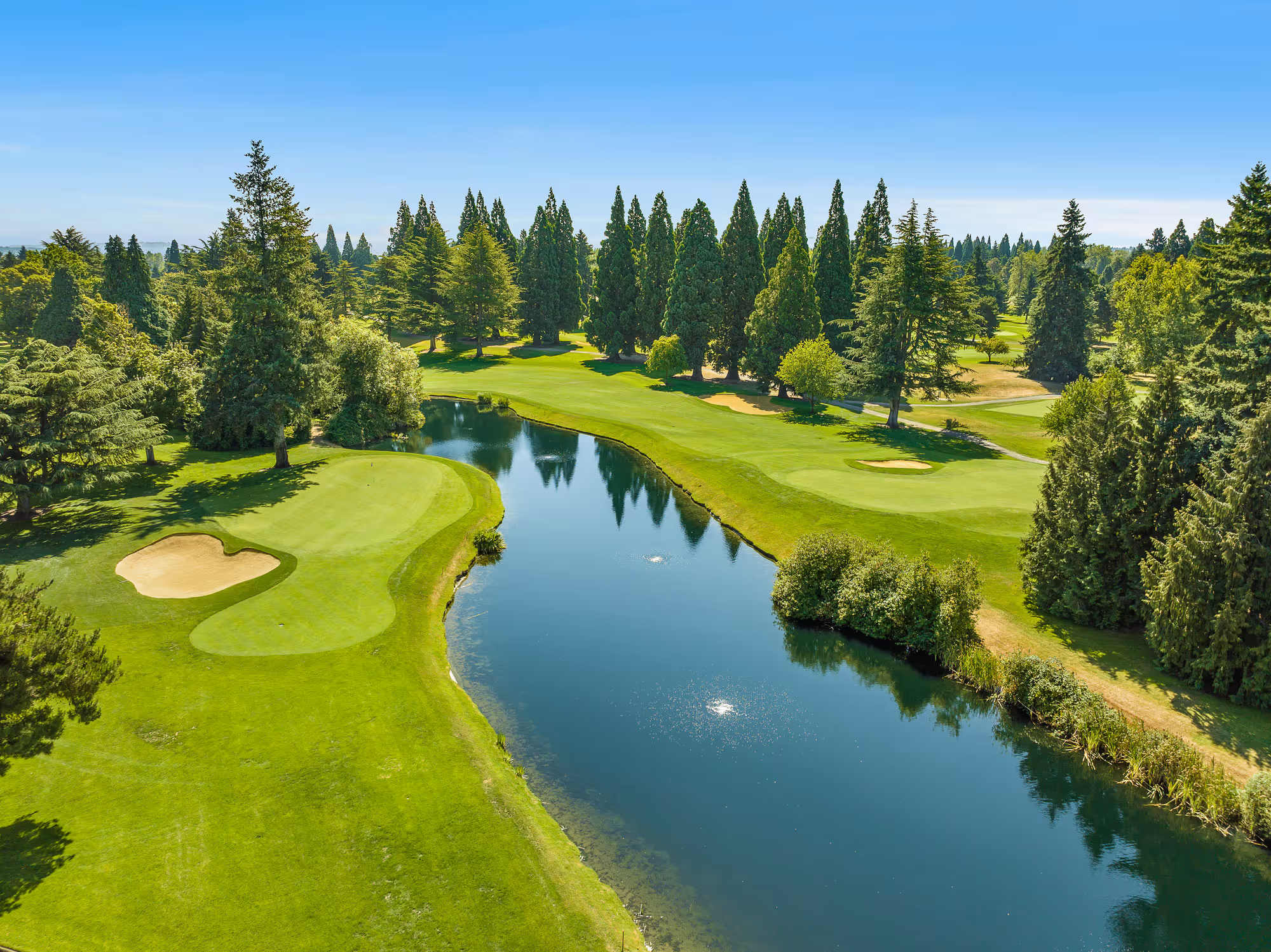 Aerial view of lush, tree-lined greens and sparkling pond of the Macan Course