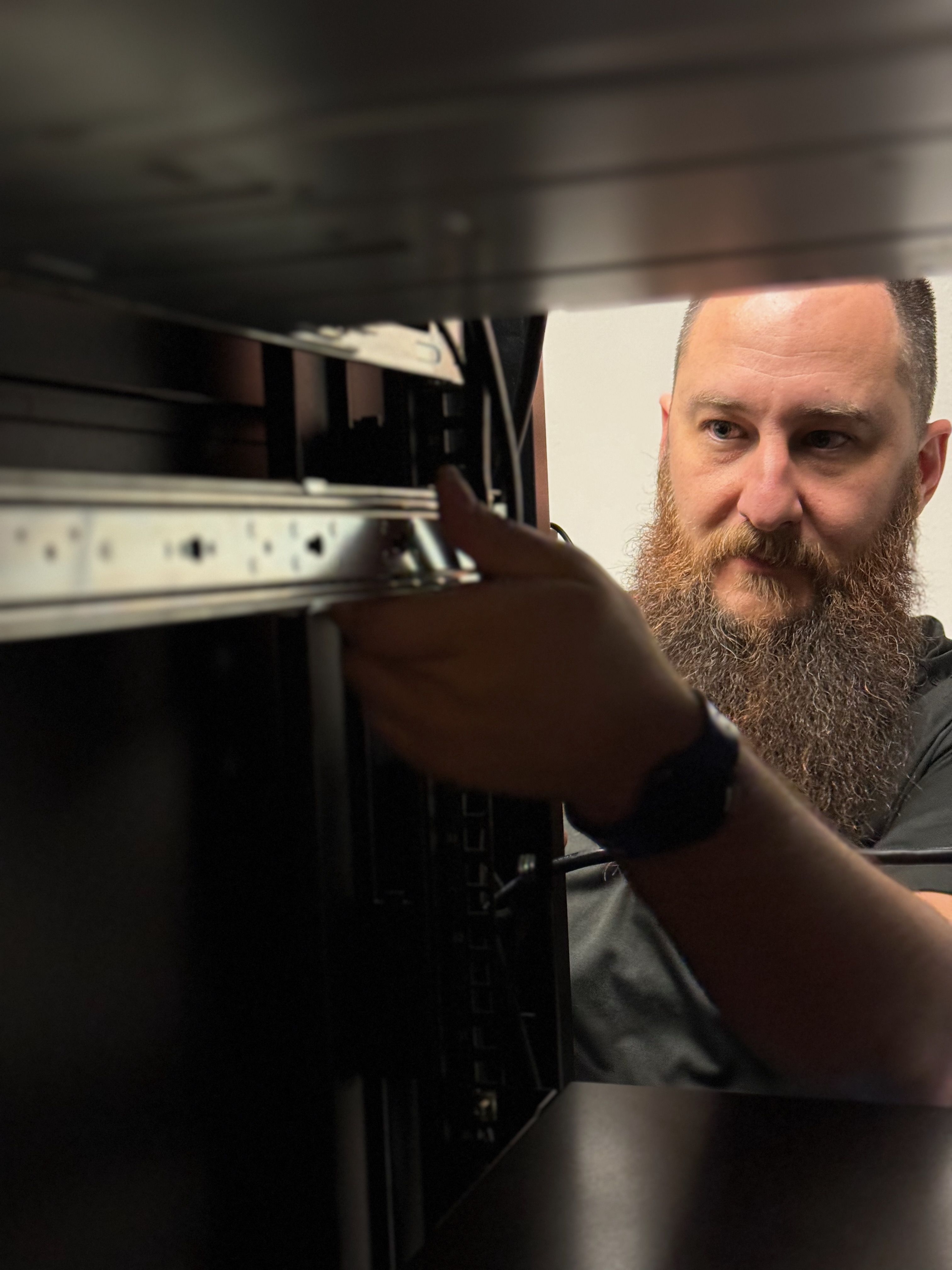 Helpdeask Director Jason Isenhart works on a server rack at a client office during an office visit, highlighting the care and expertise of Stratus staff members.