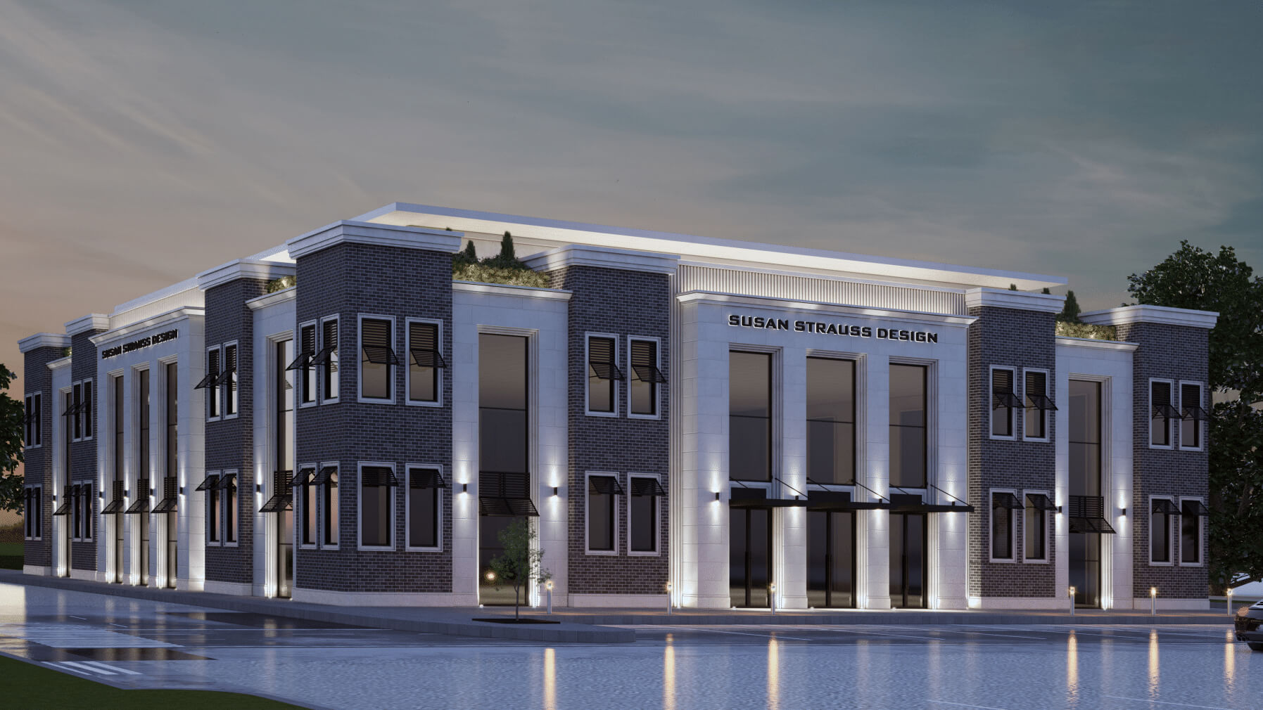 Modern two-story office building with brick and white stone facade labeled Susan Strauss Design, illuminated at dusk with reflective water in front.