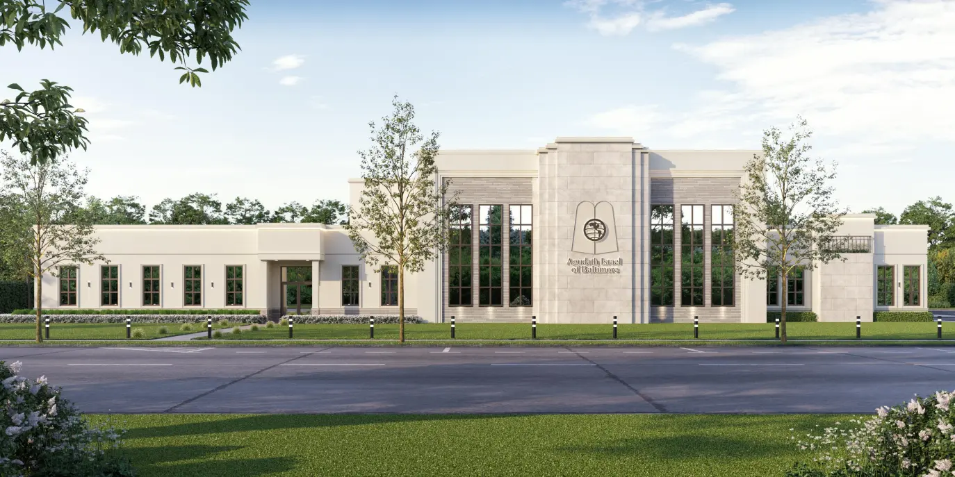 Luxurious stone mansion with steep shingled roof, large windows, and manicured garden with shrubs and white flowers under a clear blue sky.