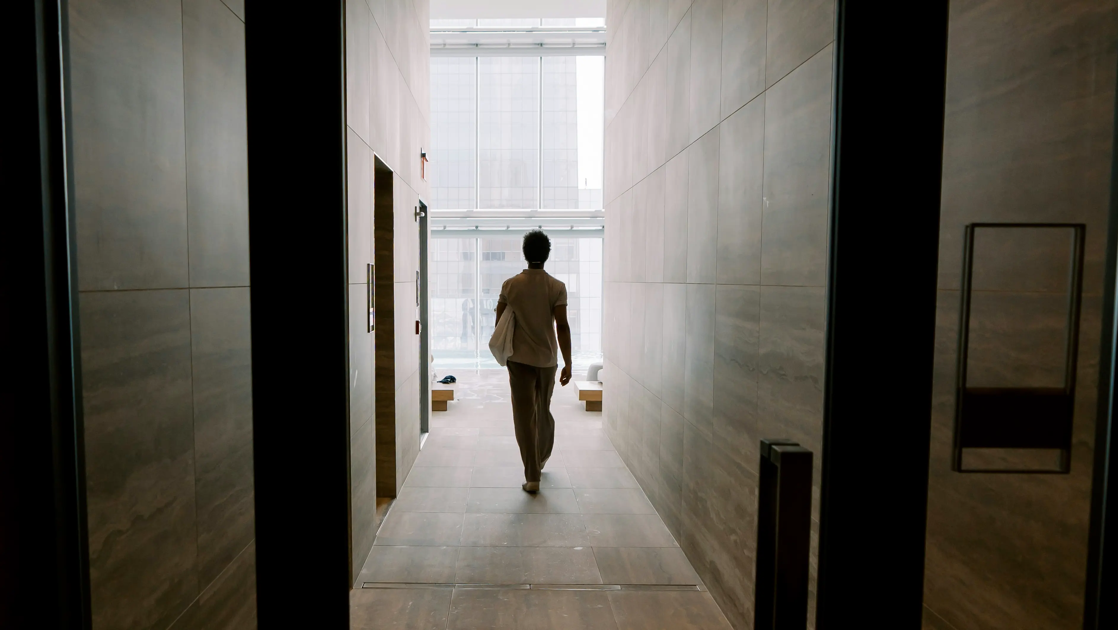A person walks through a hallway after entering a glass door.