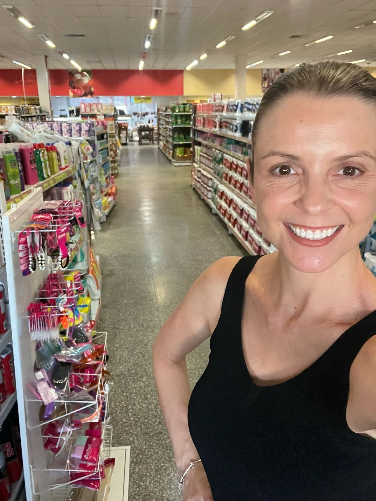 Uma foto da Diretora de Marketing do nosso cliente Supermercado Lanz, ela está de cabelo preso e uma regata preta, o fundo é do corredor do próprio supermercado.
