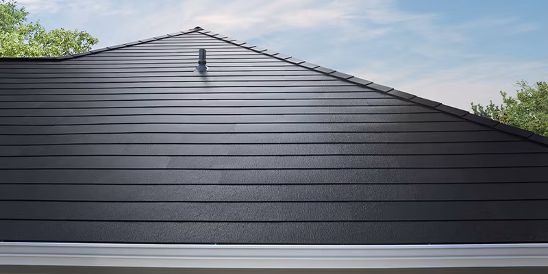 Smooth, dark metal timbersteel roof with horizontal panels and a vent pipe near the peak, set against a partly cloudy sky with green trees visible on the sides.