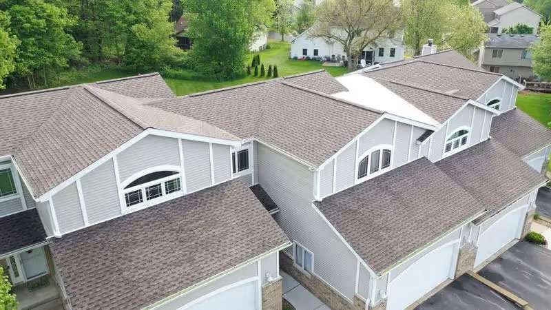 Aerial view of several attached townhouses with gray siding, brown shingle roofs, and surrounding greenery.