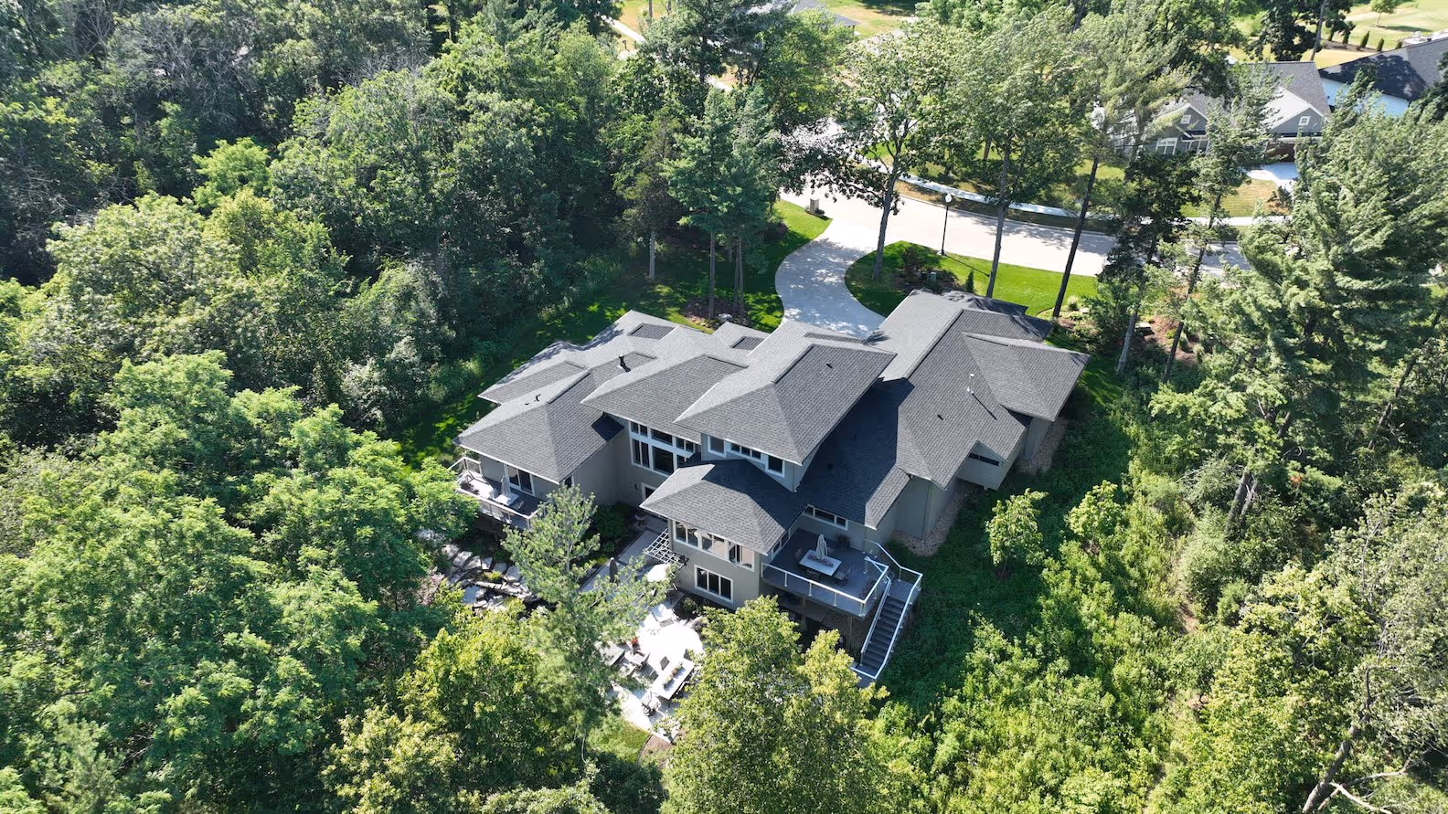 A large modern house surrounded by dense green trees and vegetation with an outdoor patio and deck.