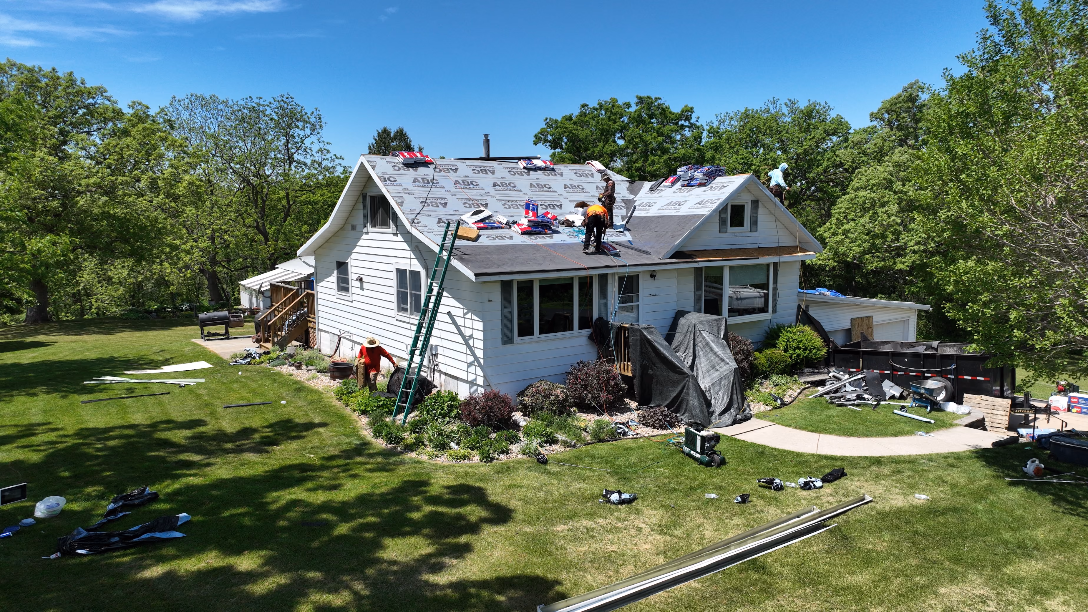 Roofing crew installing underlayment and new shingles on a white two-story home