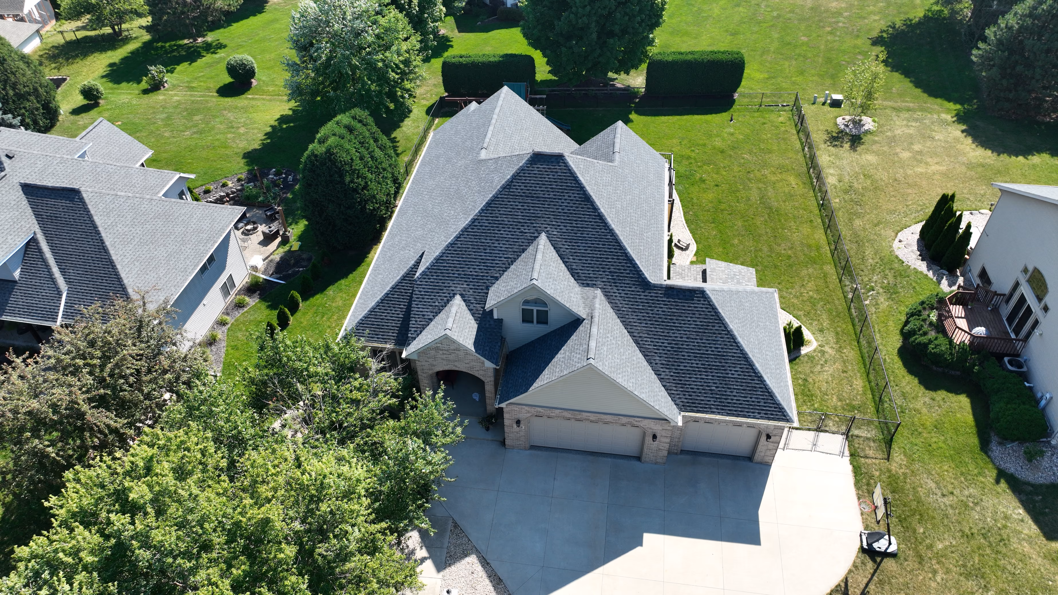 Aerial view of a Wisconsin Rapids home with a steep gray asphalt shingle roof and landscaped yard