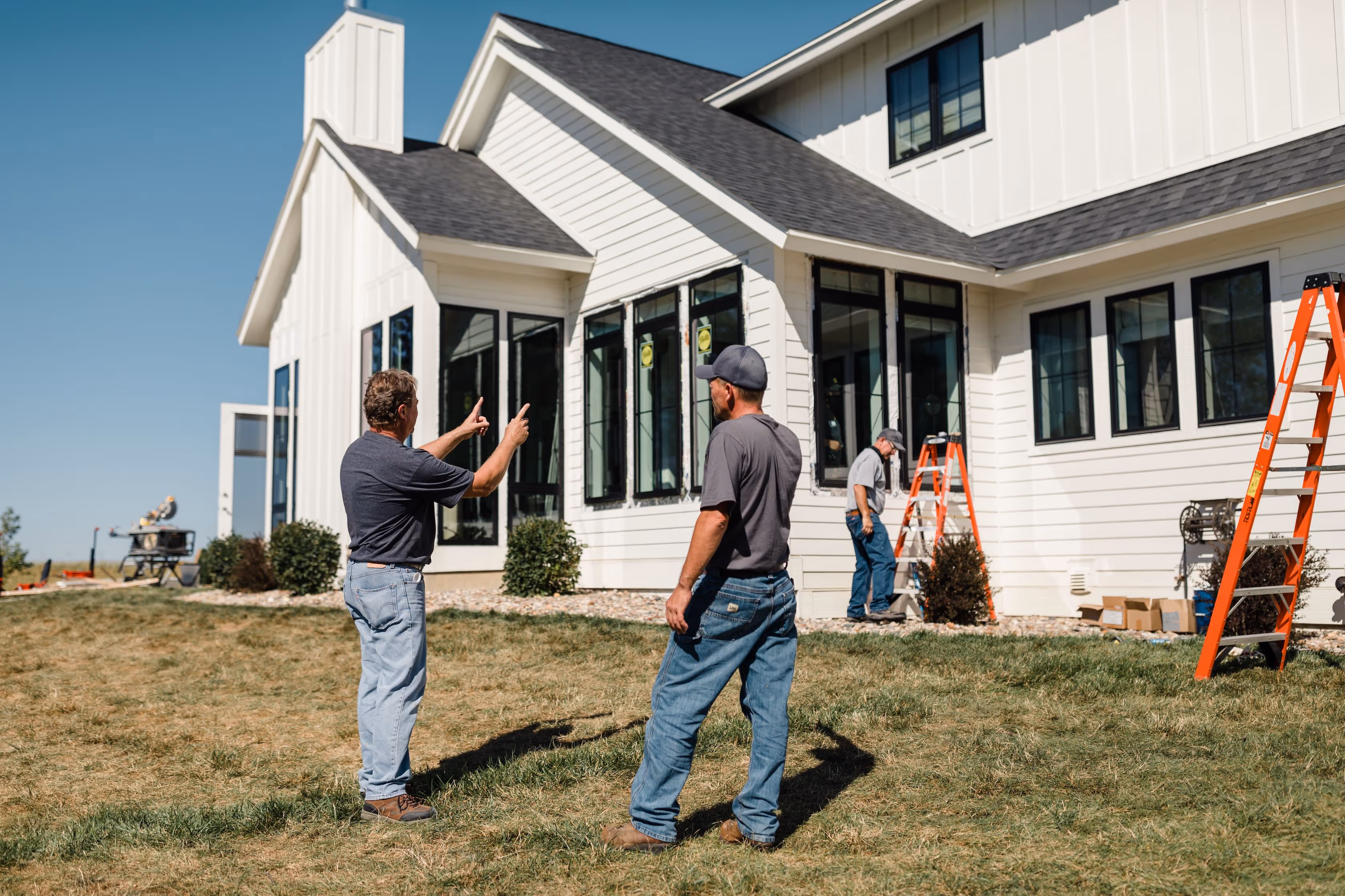 Homeowner speaking with a window installation team outside a modern white house during a replacement window project.