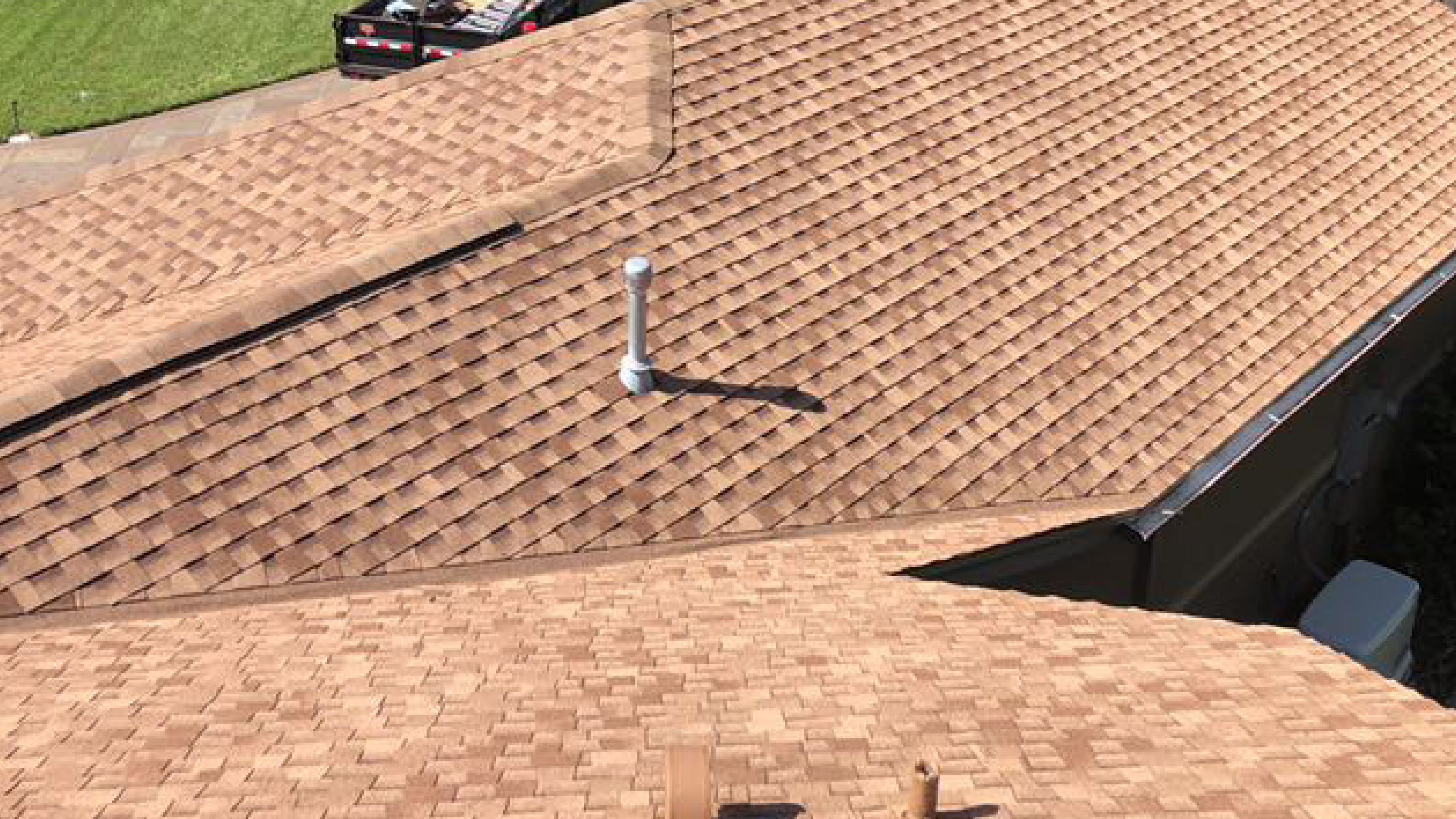 Aerial view of a tan asphalt shingle roof showing a roof valley where two slopes meet and a plumbing vent pipe, two common leak points.