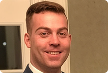 Smiling man with short brunette hair wearing a suit and tie indoors.