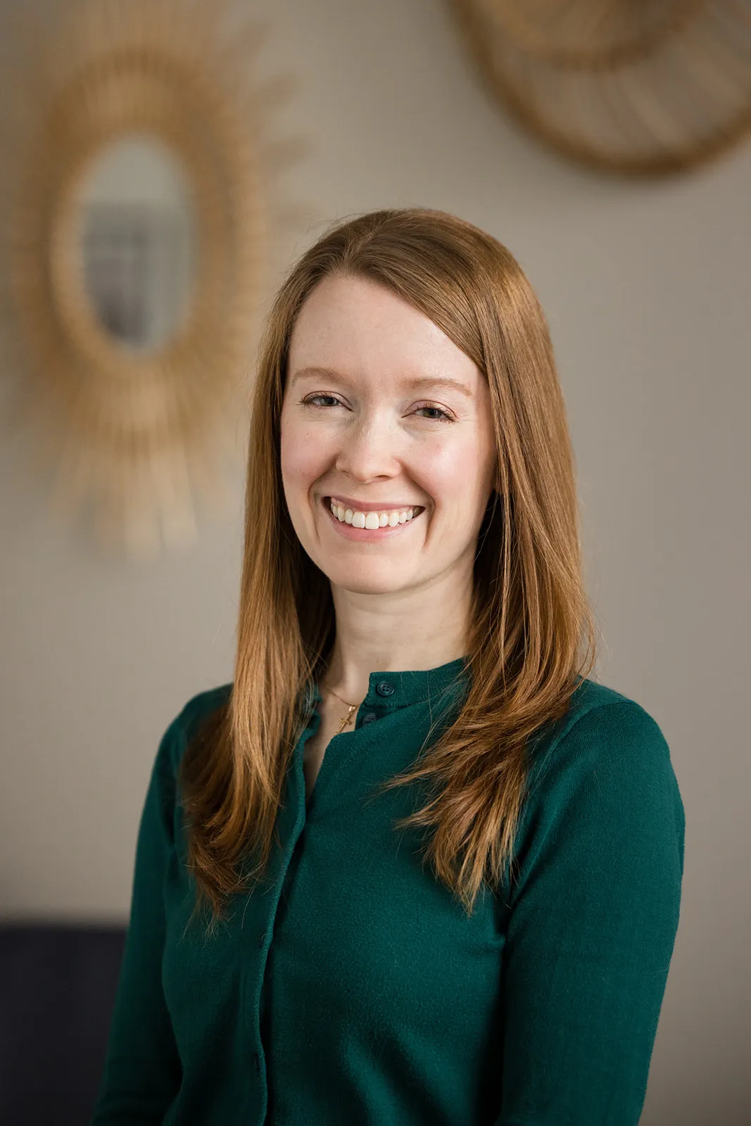 Orthodontist Dr. Maureen Wood smiling with straight reddish hair in a green buttoned top in front of blurred round wall decor.