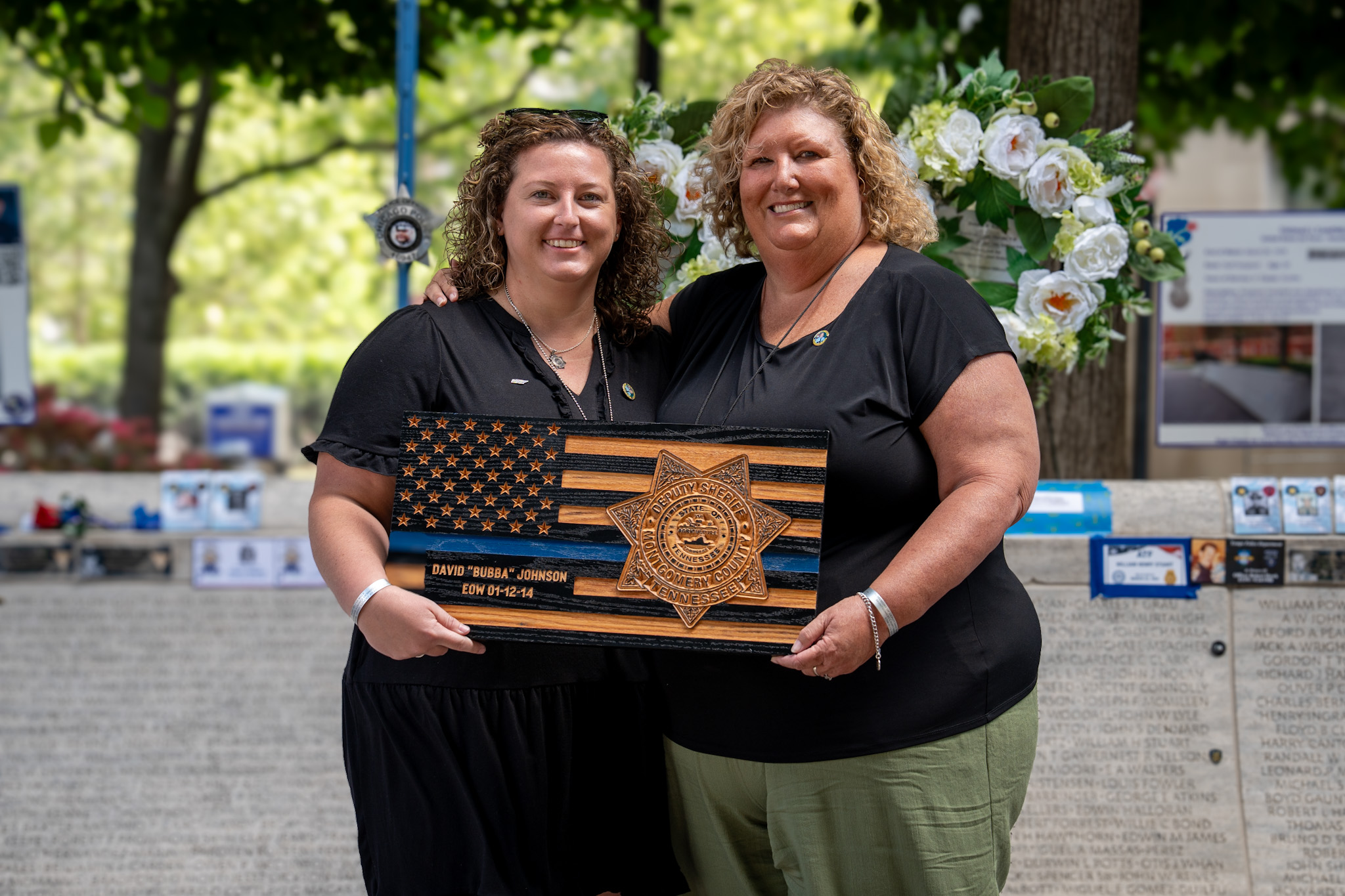 Two women holding a wooden plaque with an American flag and deputy sheriff badge for David 'Bubba' Johnson.