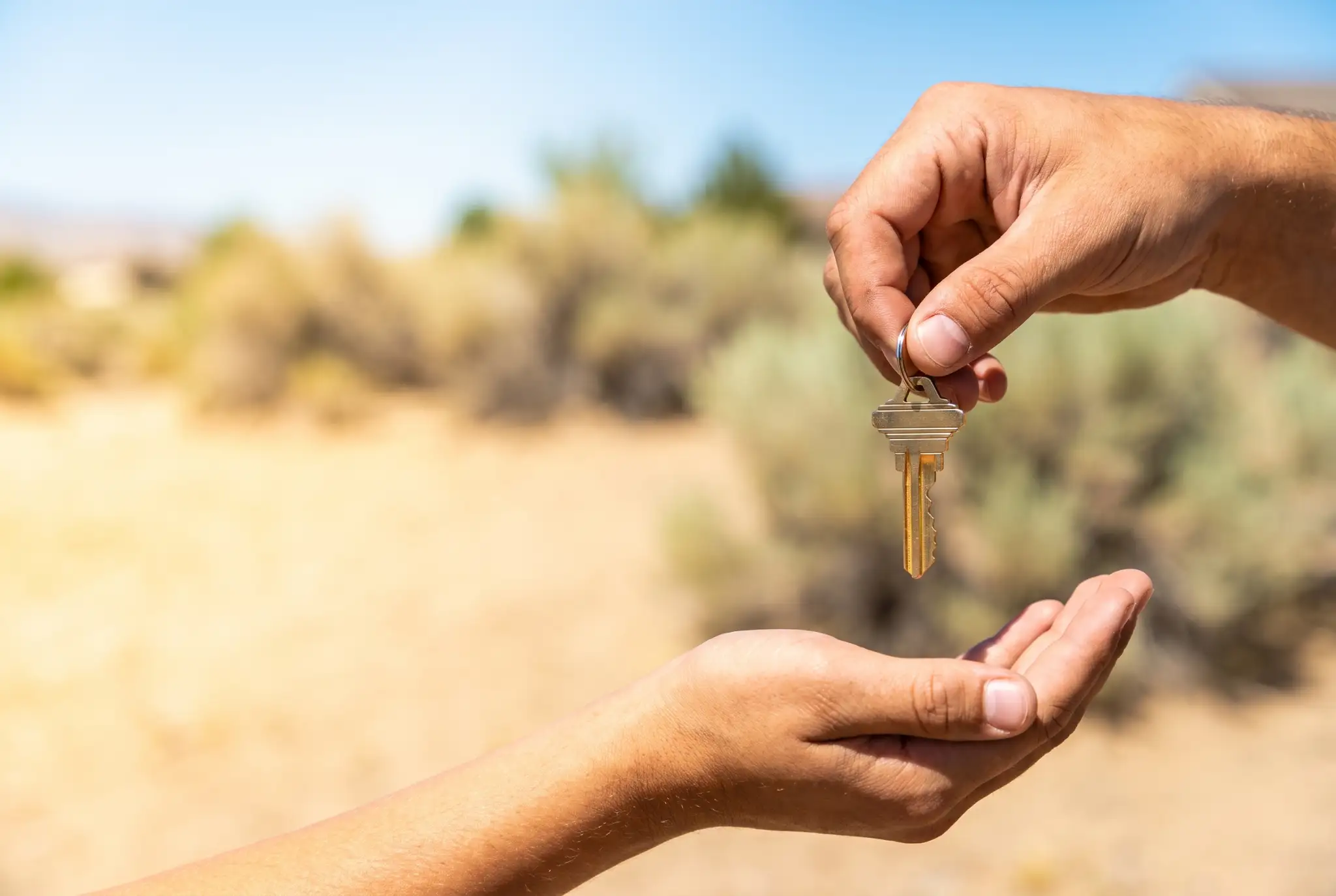 Hand passing house keys to a first-time homebuyer against a sunny Nevada desert landscape.