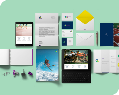 Flat lay of branded stationery and digital devices including tablets, letterhead, business cards, notebooks, and envelope on a green background.