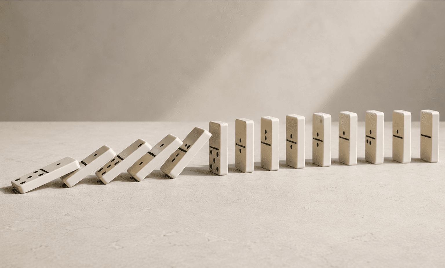 A row of white dominoes, some falling and some standing, on a smooth beige surface.
