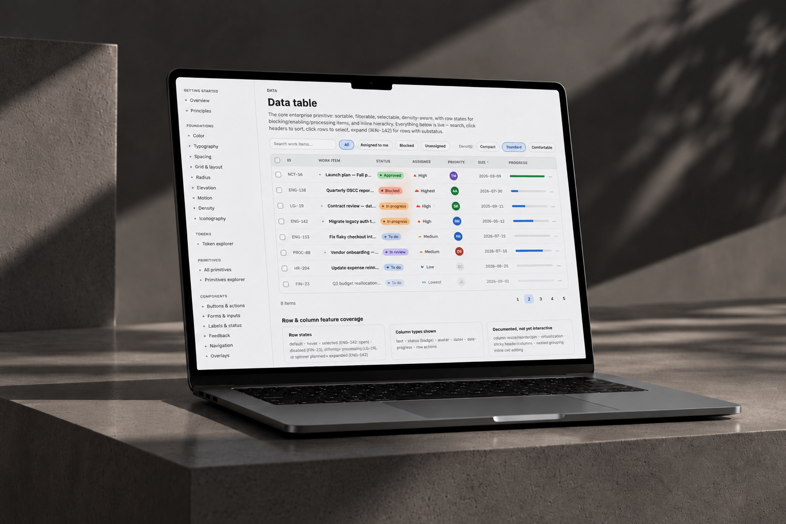 Enterprise design system UI kit displayed on a laptop, showing foundations, tokens, primitives and components sidebar with a live data-table component.