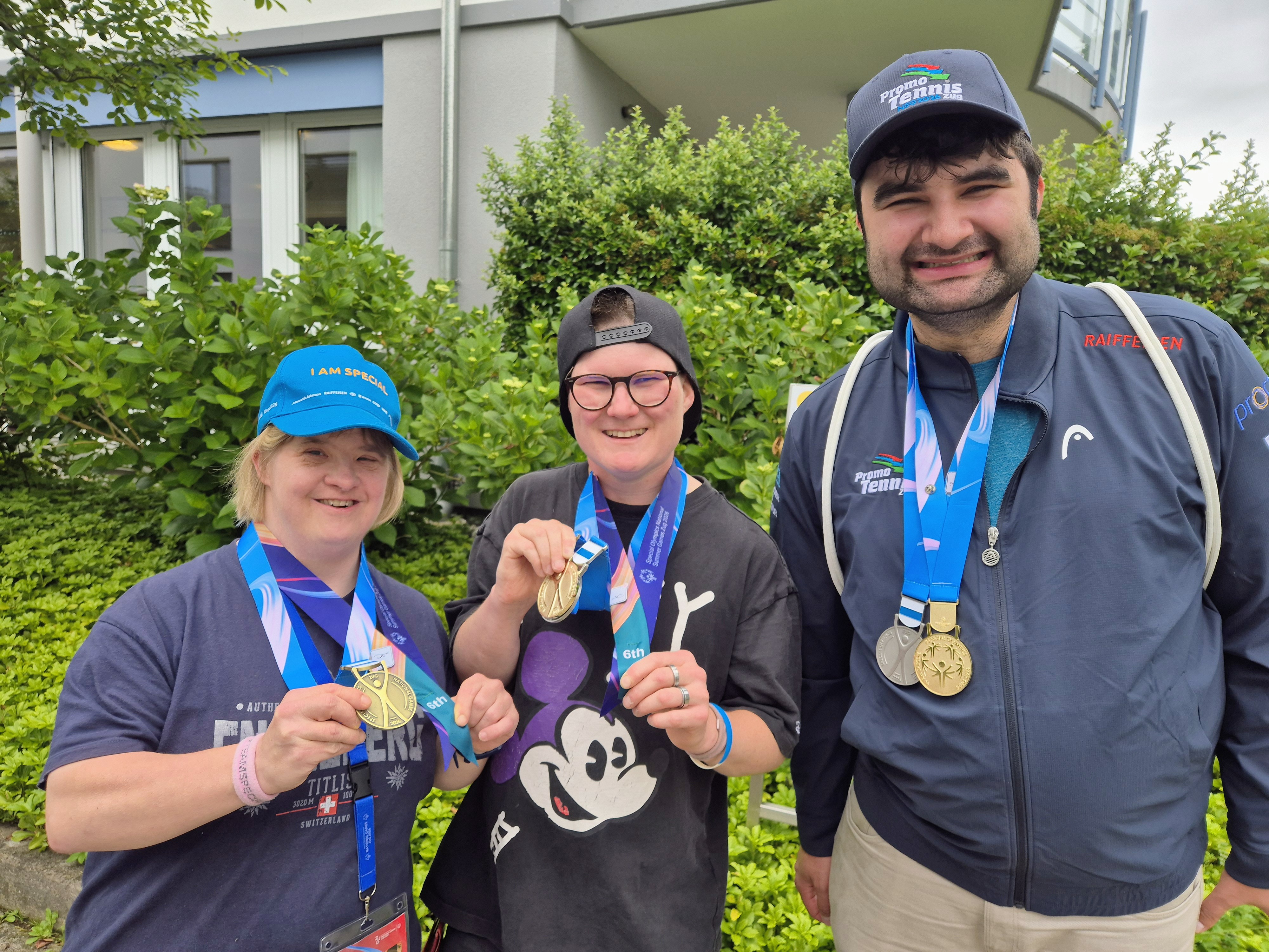 Drei Sportlerinnen und Sportler zeigen ihre Medaillen der Special Olympics