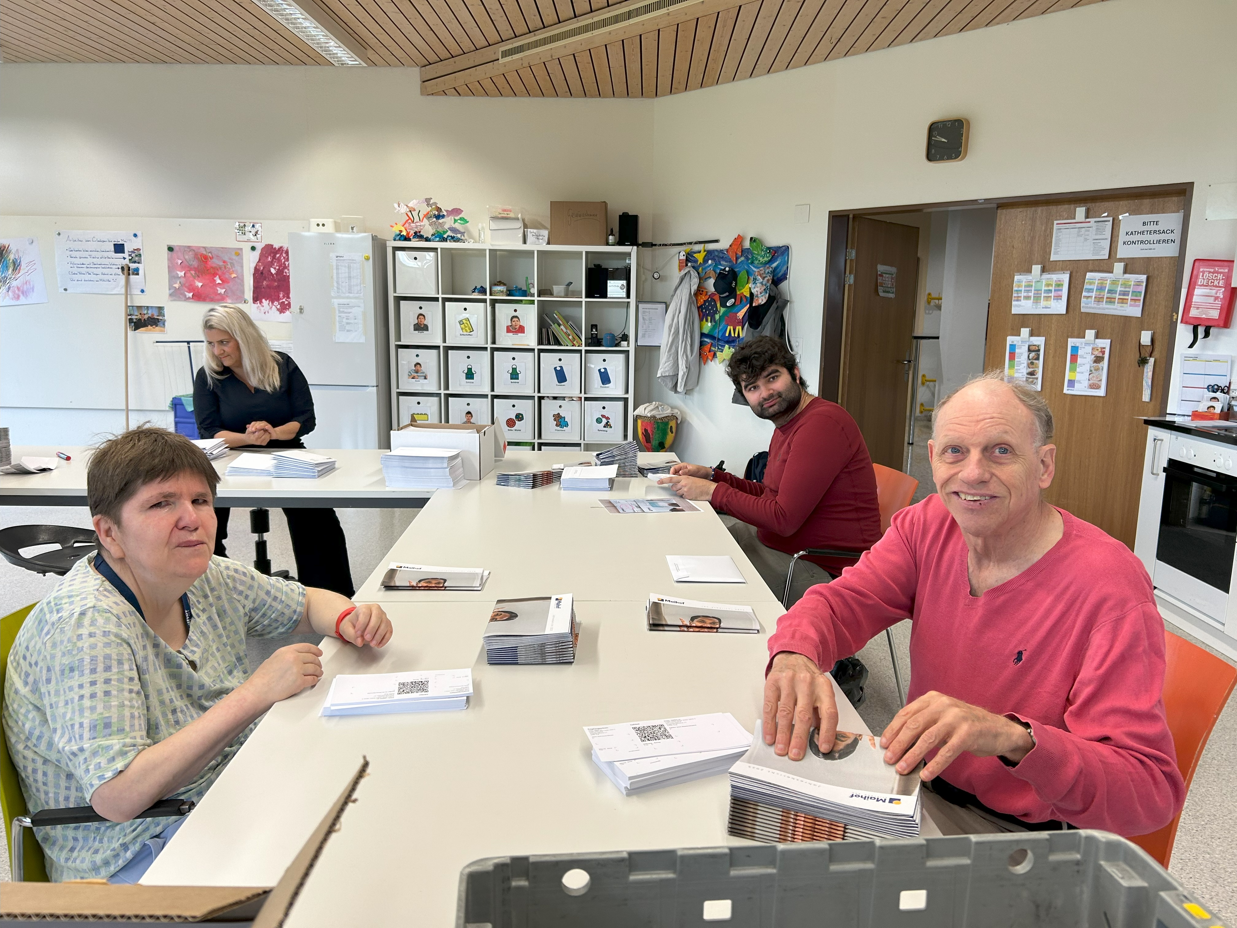 Klientinnen und Klienten verpacken Jahresberichte an einem langen Tisch im Atelier