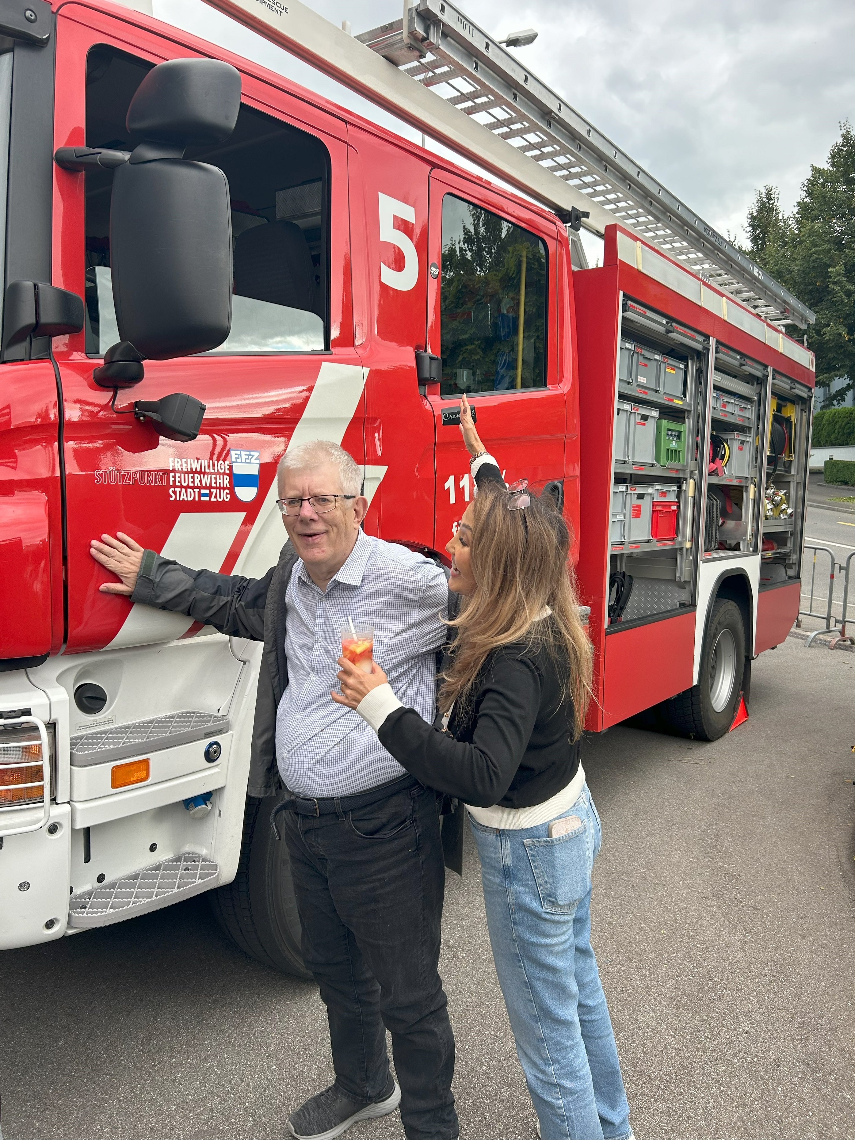 Mann und Frau mit Getränk posieren vor einem Feuerwehrauto
