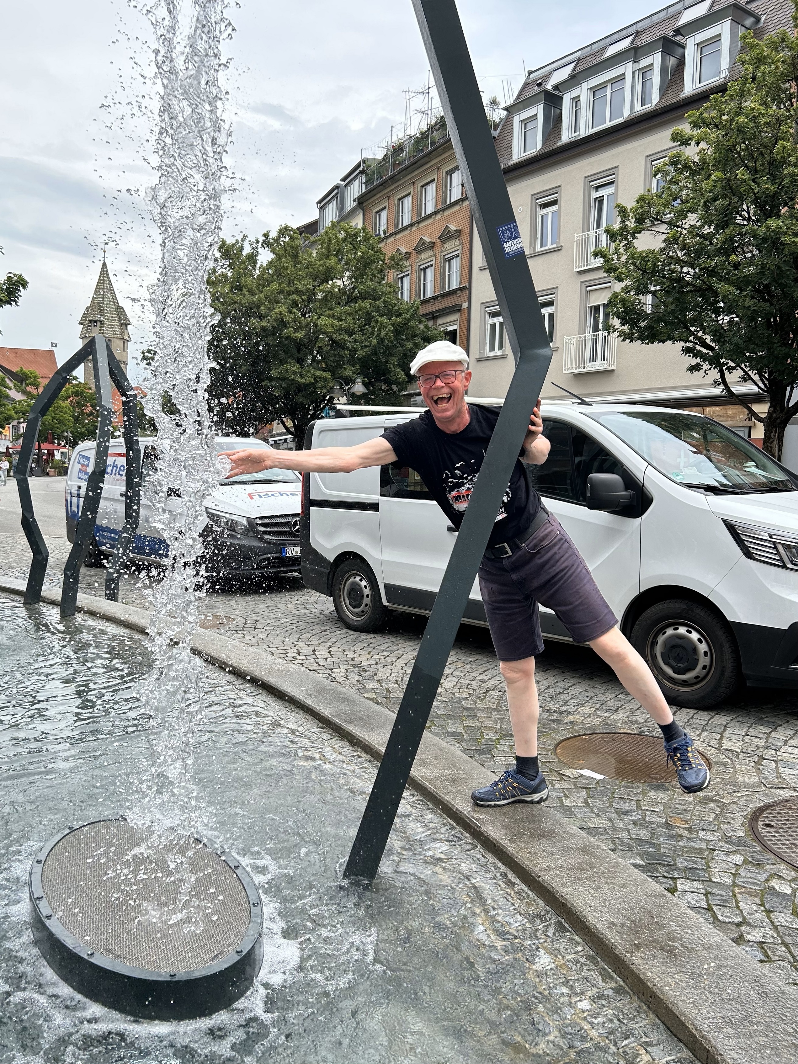 Mann springt fröhlich neben einem Wasserspiel in einer Altstadt
