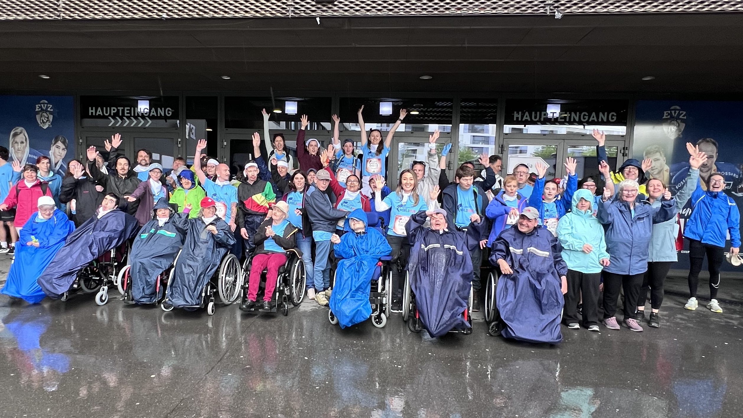 Grosse Gruppe in Regenponchos jubelt vor einem Stadion beim Wings for Life-Lauf
