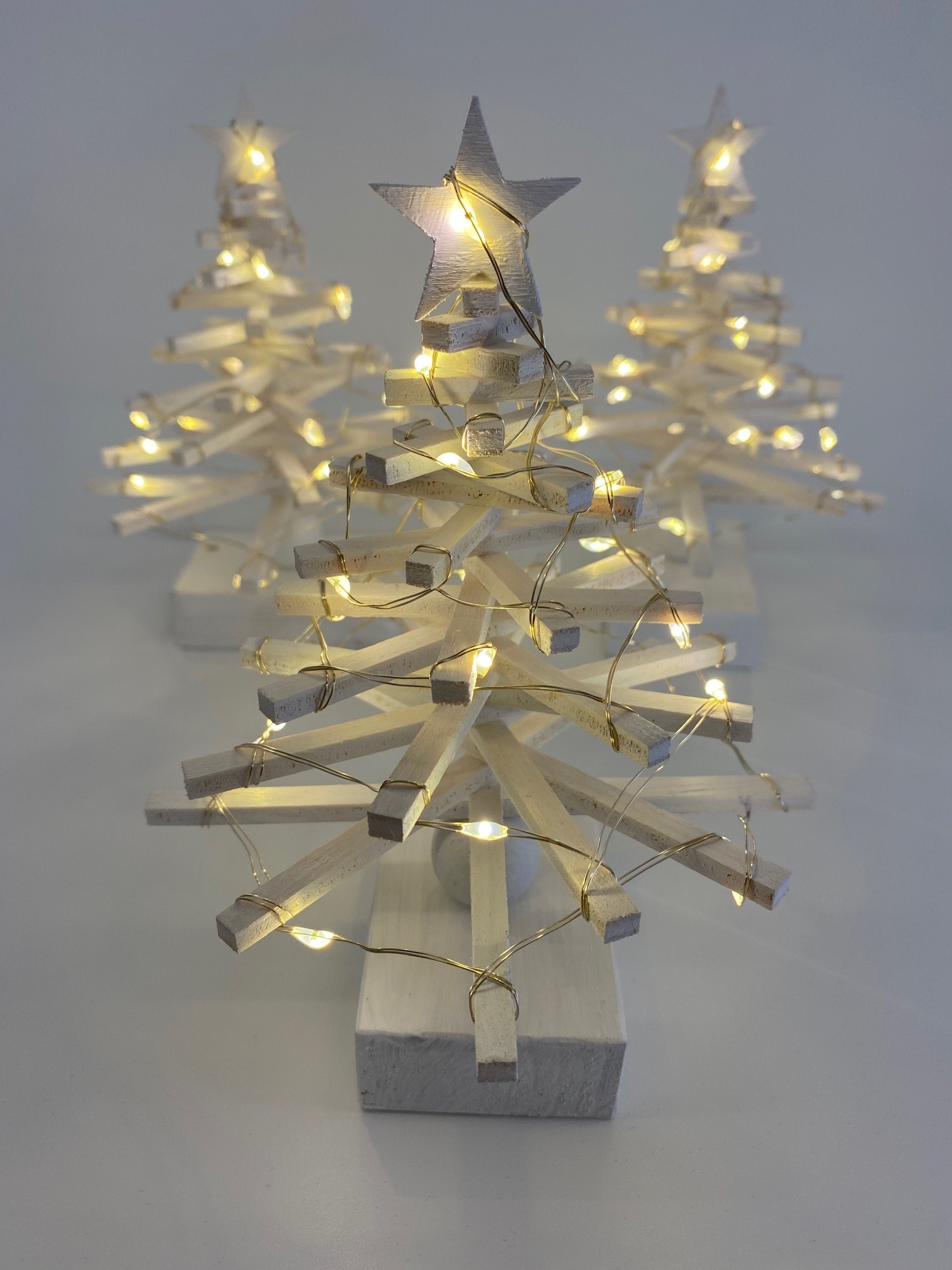 Beleuchtete Weihnachtsbäume aus Holzleisten mit Lichterkette