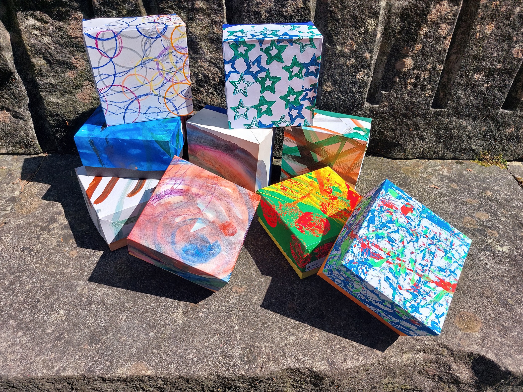 Von Hand bemalte Geschenkschachteln in vielen Farben auf einer Steinmauer