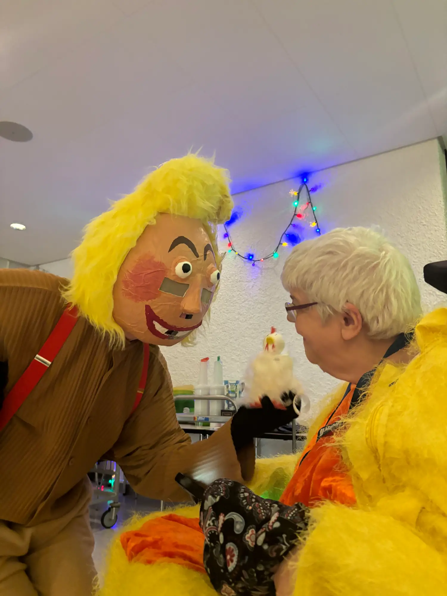 Fasnacht: Person mit gelber Perücke und Maske begrüsst eine verkleidete Frau