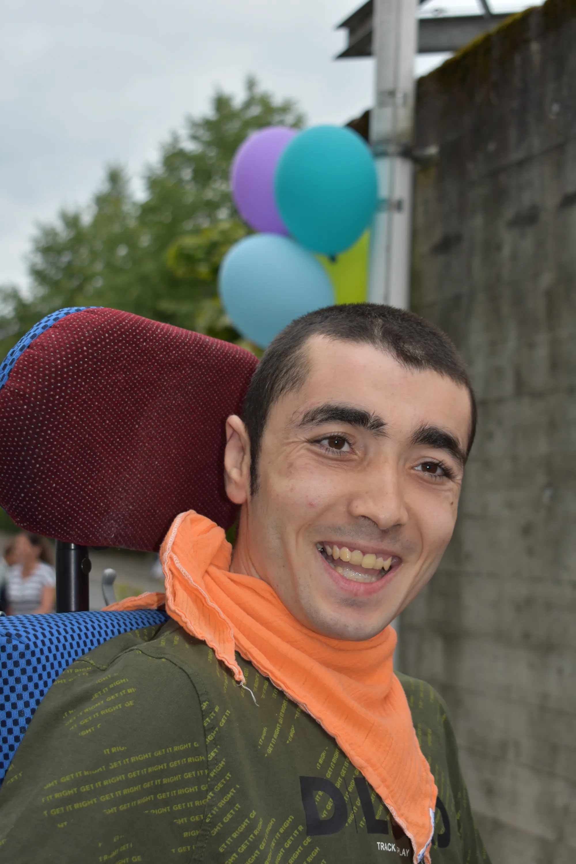Junger Mann mit orangem Halstuch lacht am Sommerfest