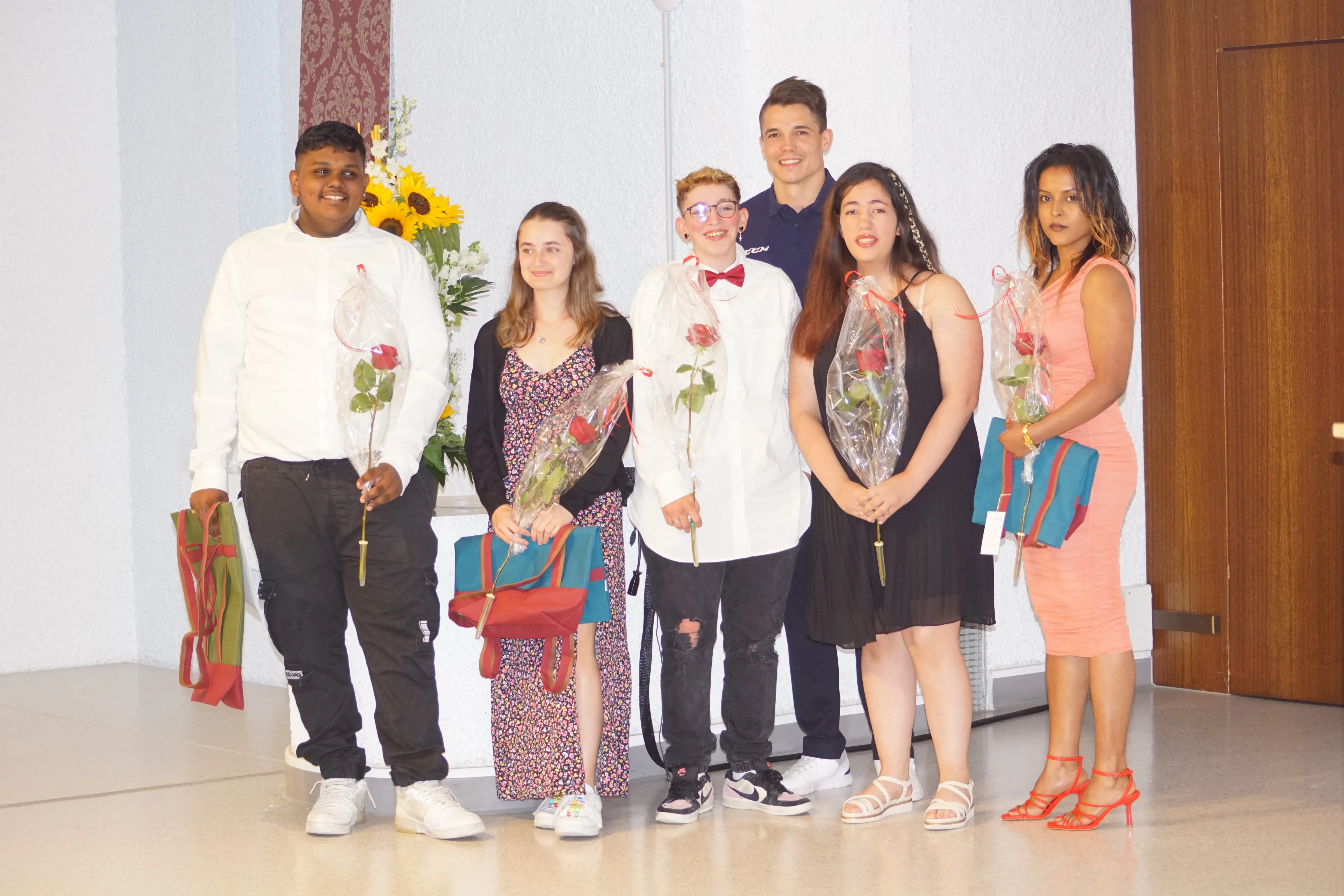 Sechs Lernende mit Rosen und Geschenken bei der Abschlussfeier