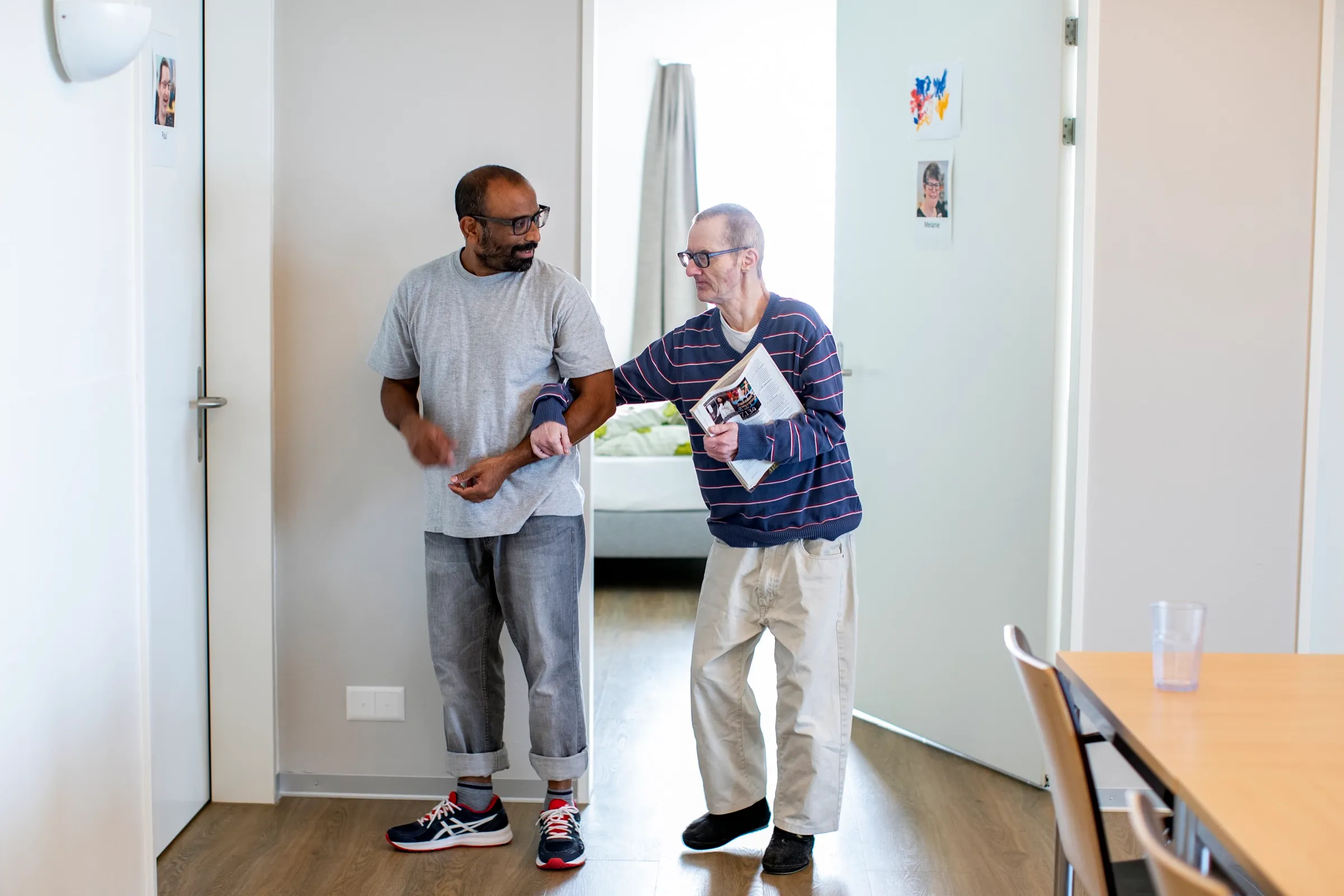 Zwei Männer gehen untergehakt durch einen Gang im Wohnhaus