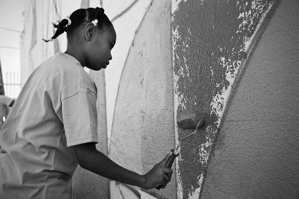 Menina pinta um mural com rolo de tinta em projeto de impacto social, em preto e branco