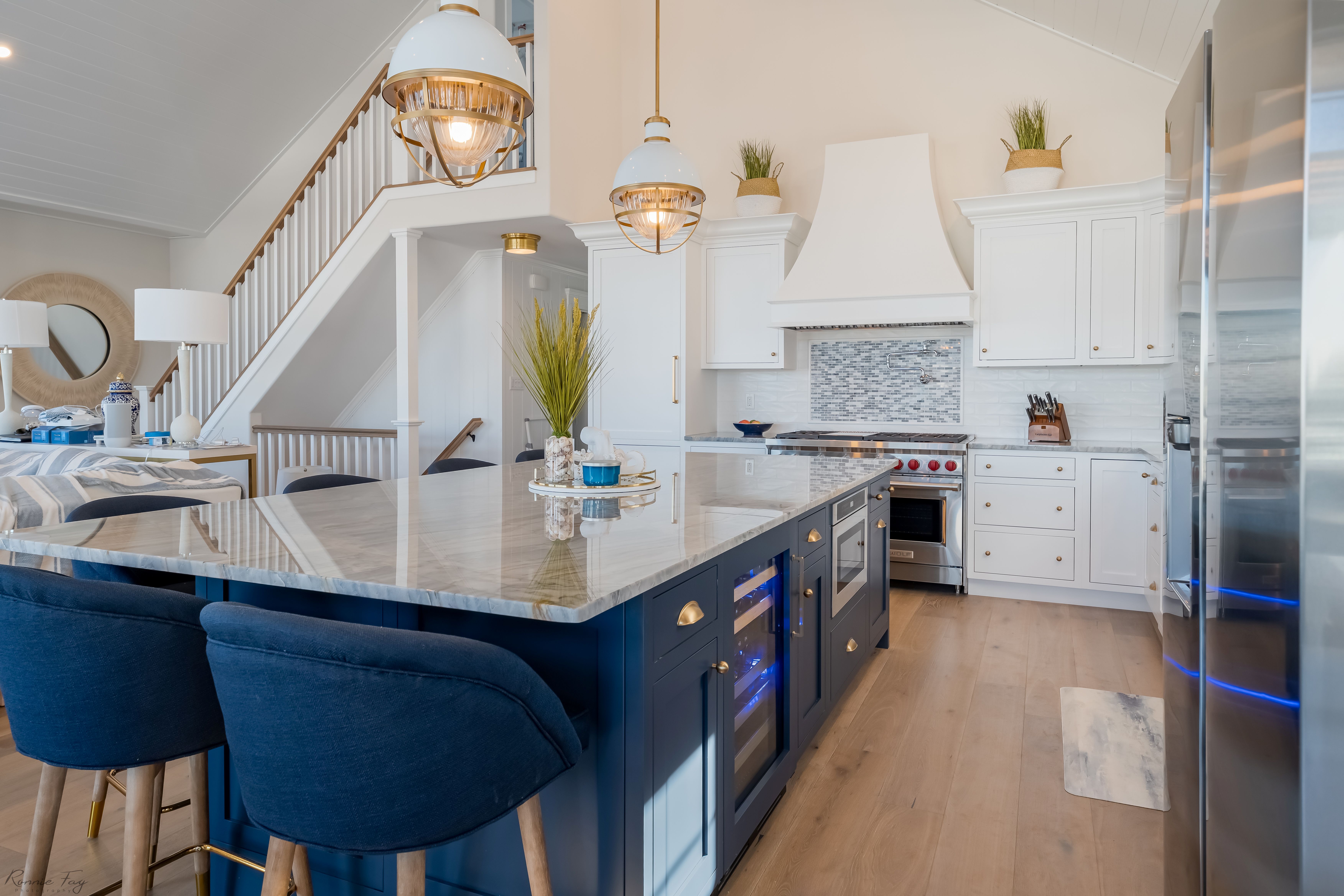 A kitchen with white top cabinets, blue lower cabinets, blue chairs, and a wooden floor.