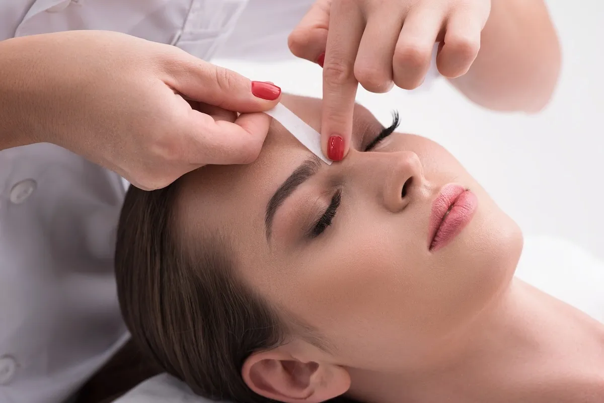Esthetician shaping a client's eyebrow with wax