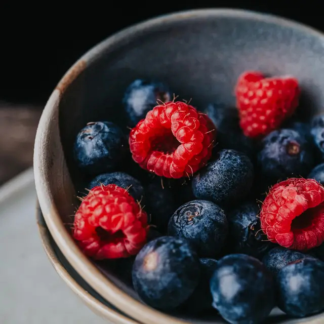 Fruits en macro, framboises et myrtilles dans une coupe en céramique.