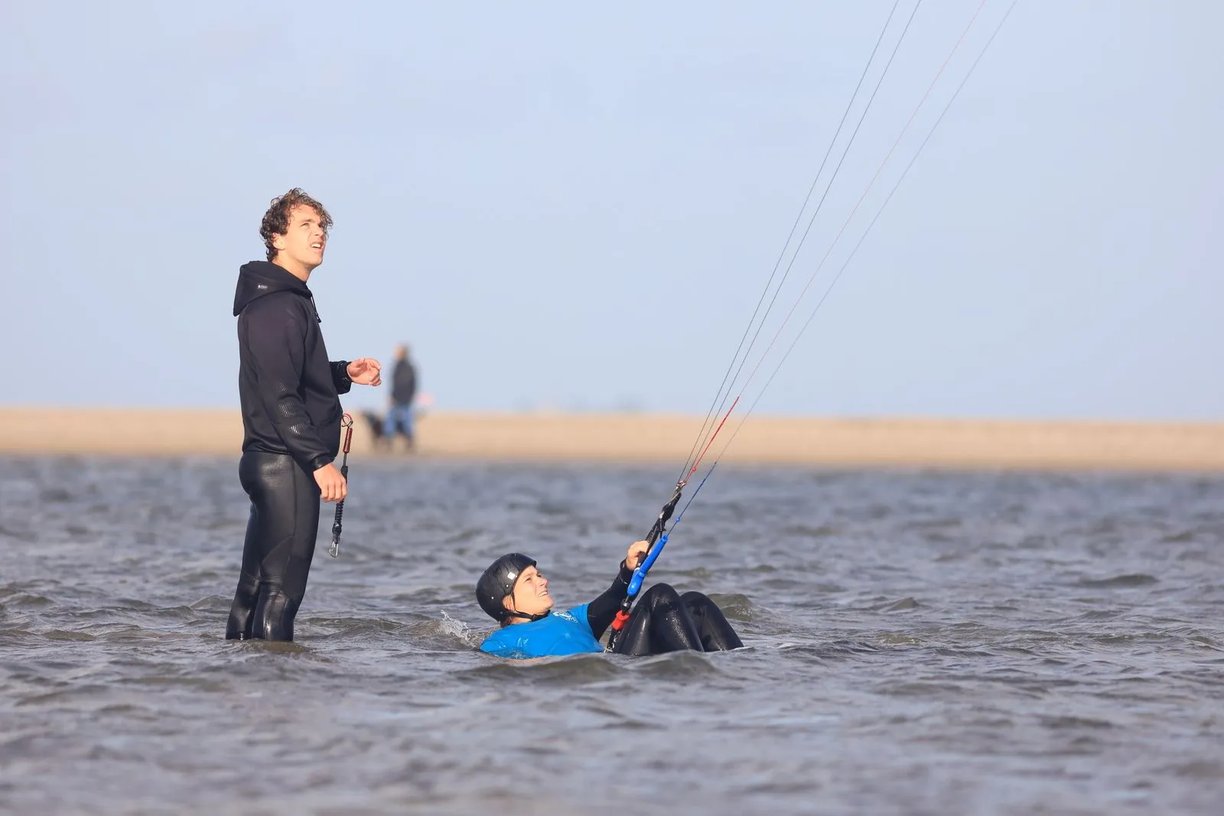 Beginner leert kitesurfen met instructeur op het strand van Scheveningen