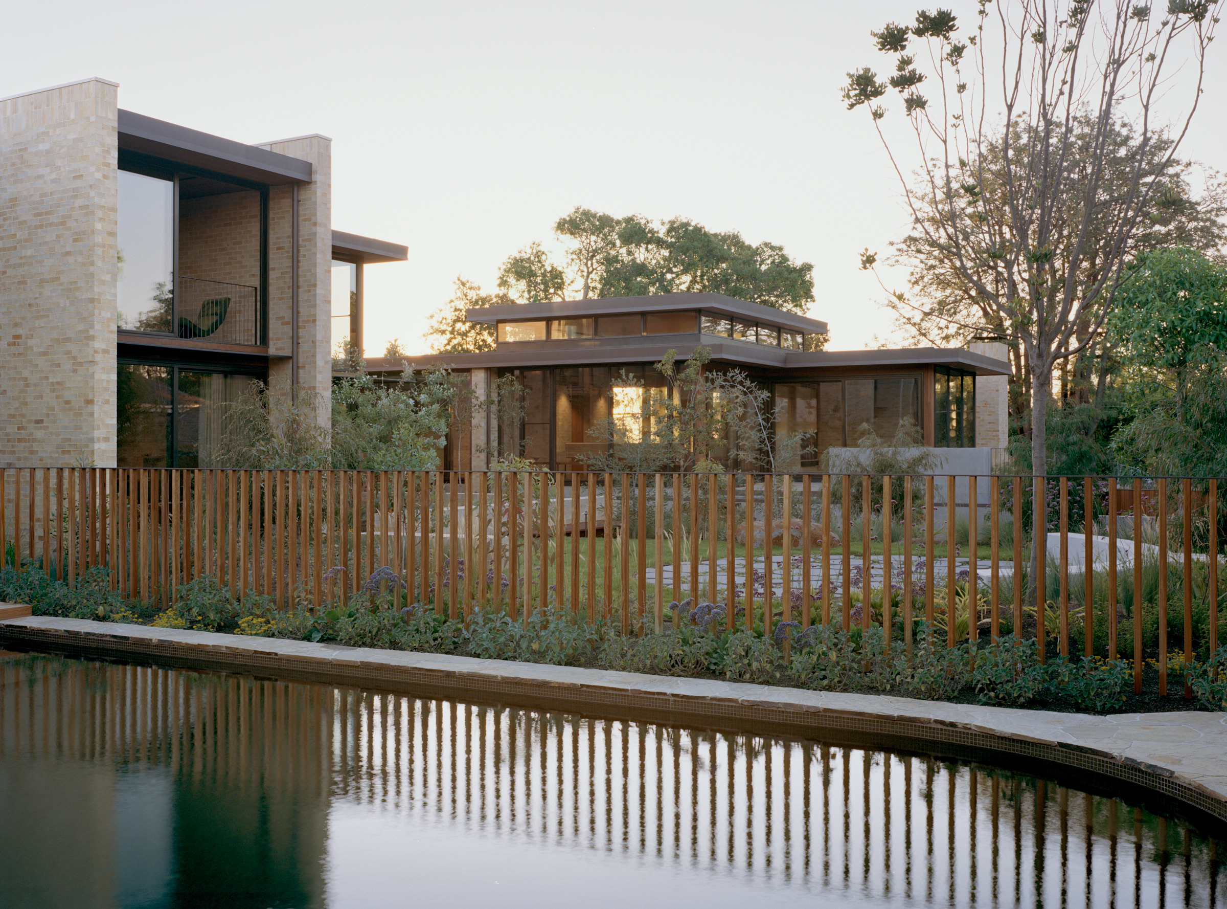 Ora House at dusk with illuminated glazing beside the swimming pool.