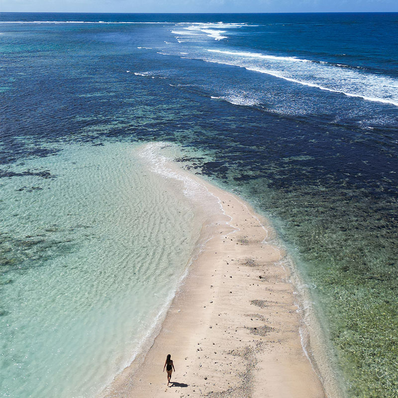 A lady walking along a sand bar surrounded by the lagoon