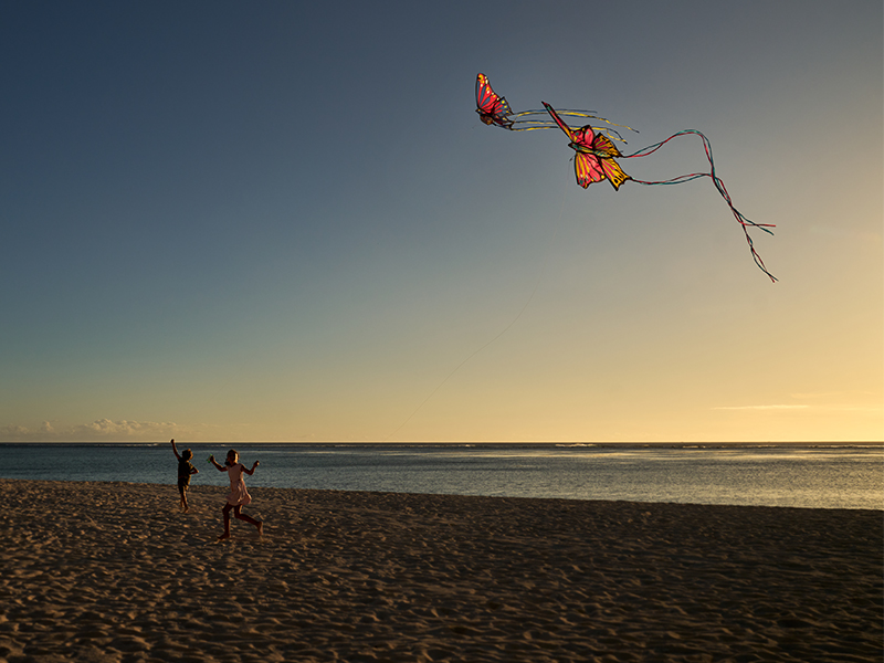 Two kids flying kites on the beach at sunset