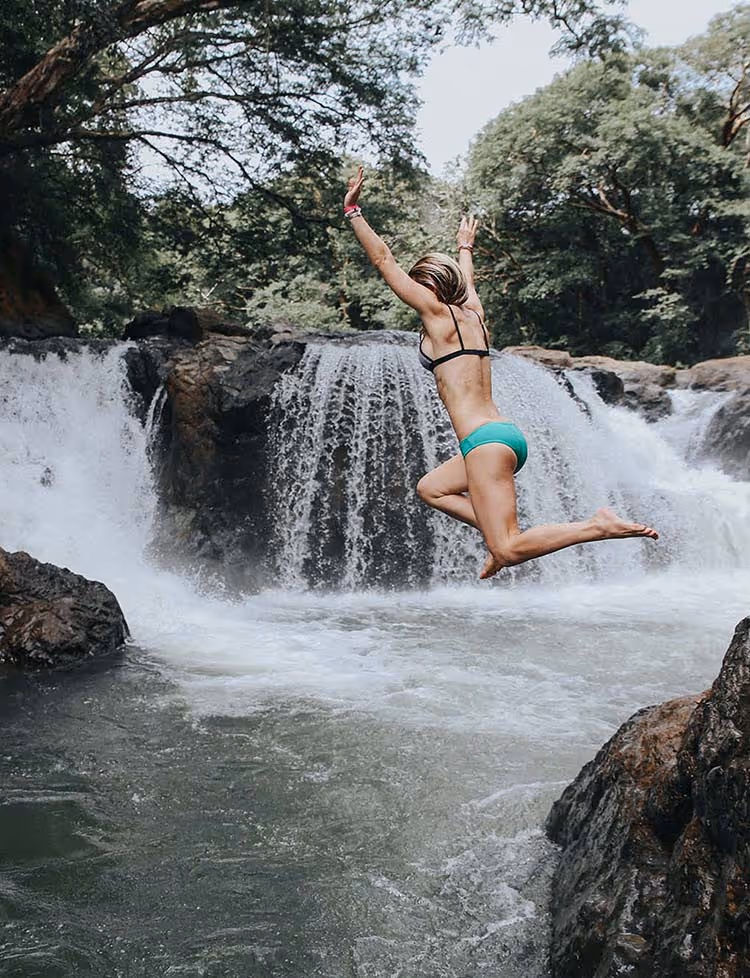 Woman jumping off cliff into waterfall on an excursion in Costa Rica